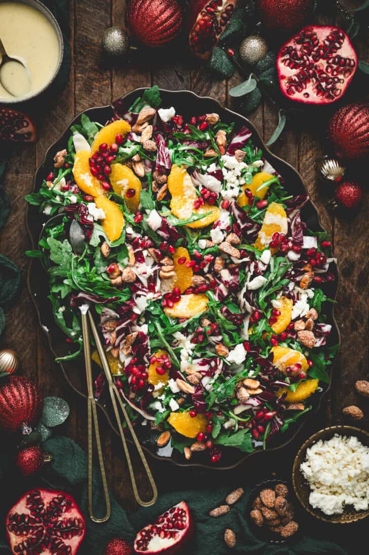 A large oval platter filled with Christmas salad, with serving utensils placed along the side.