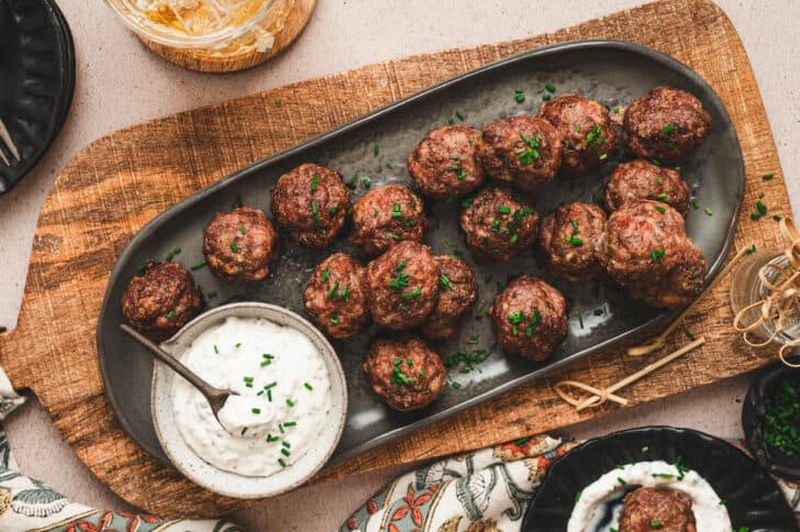 An oval gray platter topped with a party meatball recipe and a bowl of creamy sauce.