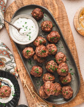 An oval gray platter topped with cocktail meatballs and a bowl of creamy sauce.
