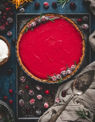 A cranberry curd tart garnished with sugared cranberries on a textured baking pan.