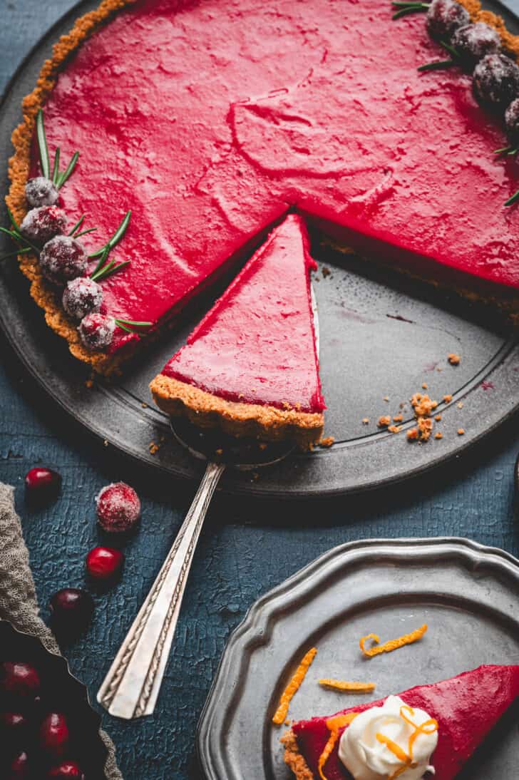 A pie serving removing a piece of cranberry custard tart from the a serving plate.