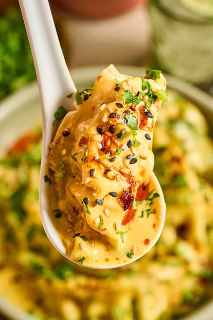 A spoon lifting up a bite of baked dumplings covered in creamy sauce.