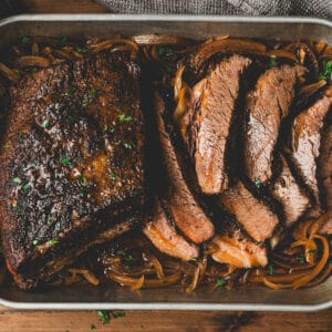 A roasting pan full of a brisket in the oven recipe, with some of it sliced.