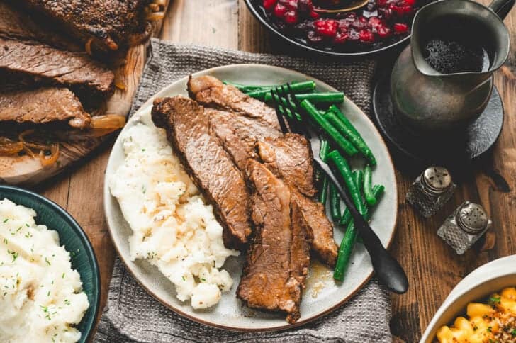 Sliced oven brisket on a plate with mashed potatoes and green beans.