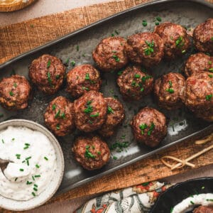 An oval gray platter topped with cocktail meatballs and a bowl of creamy sauce.
