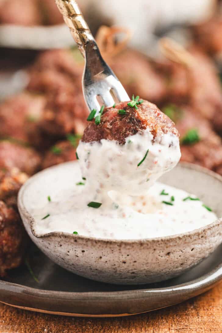 A fork dipping a meatball into a creamy meatball appetizer sauce.