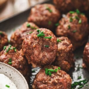 A closeup photo of cocktail meatballs sprinkled with chives.