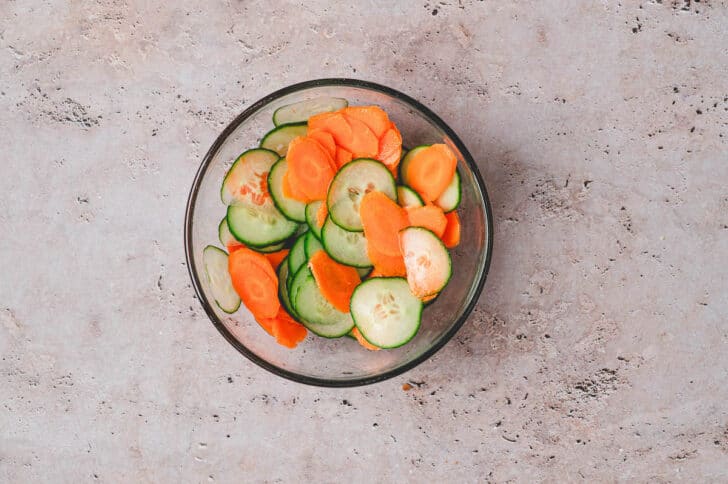 A glass bowl filled with sliced cucumbers and carrots.