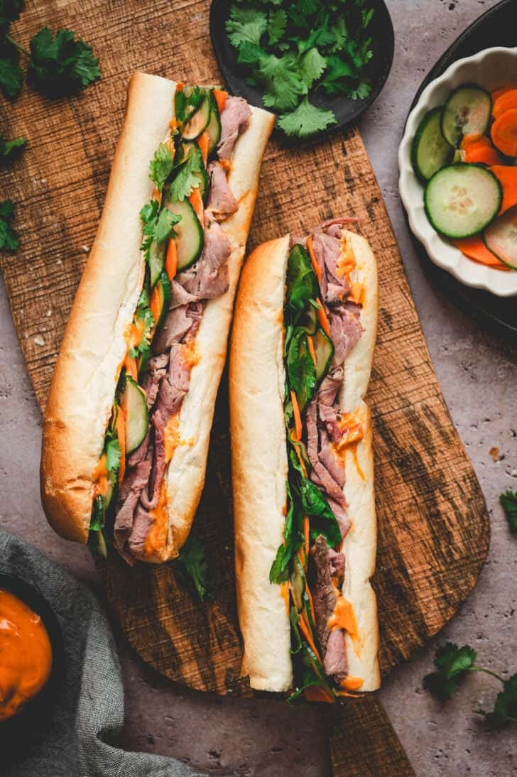 Two rib roast sandwiches made with pickled vegetables, on a wooden board.