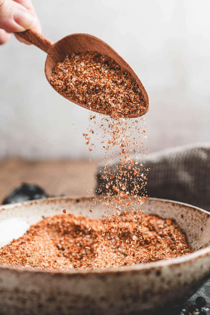 A wooden scoop sprinkling the best brisket rub into a bowl.