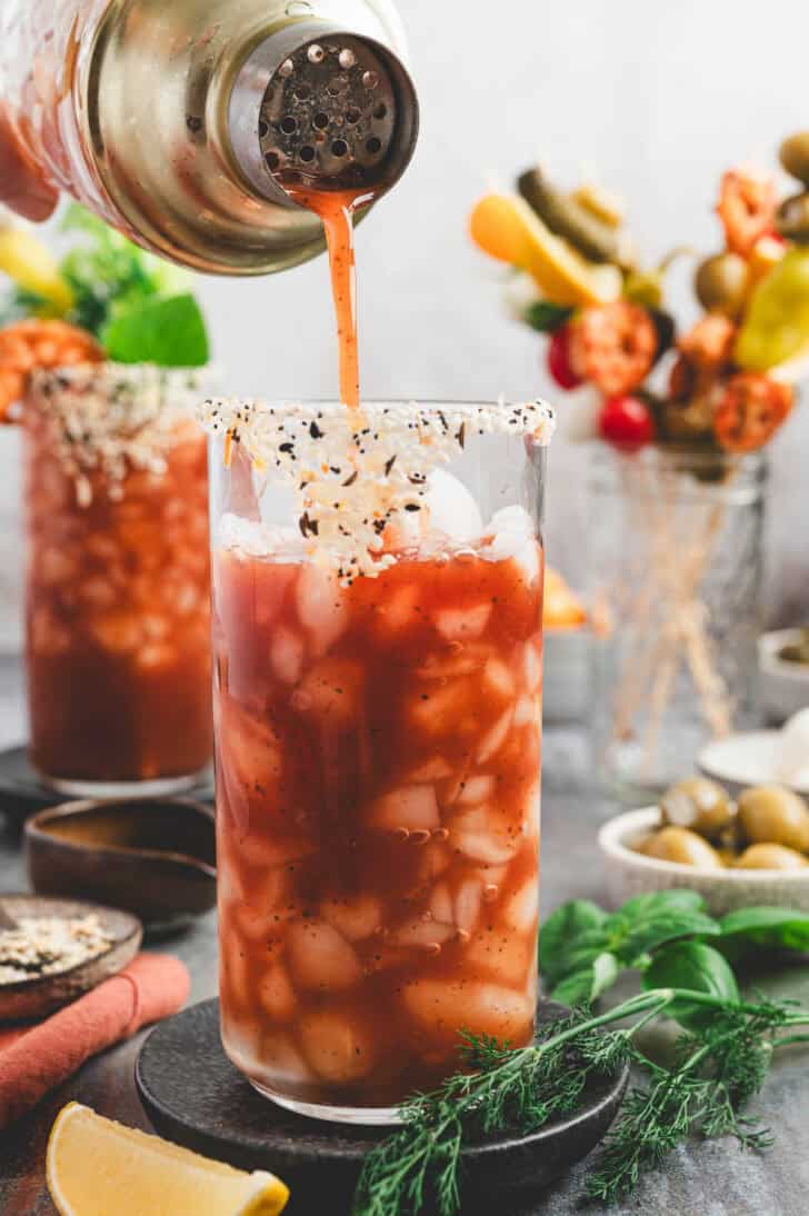 A cocktail shaker pouring bloody mary mix over ice.