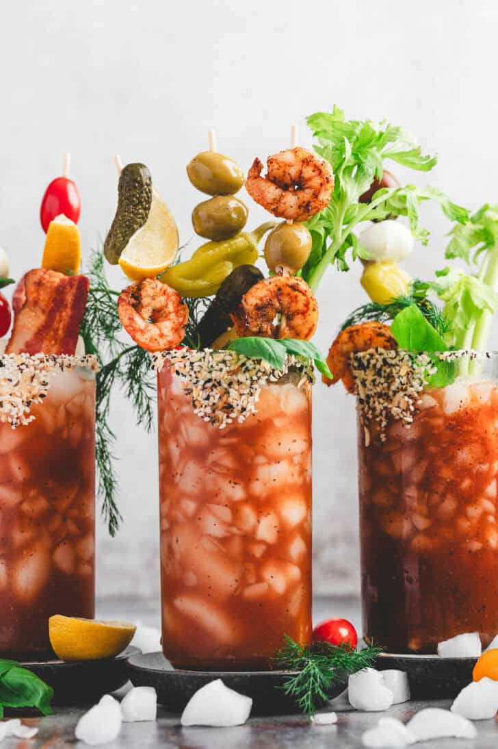 Three red cocktails with bloody mary garnish skewers in them.