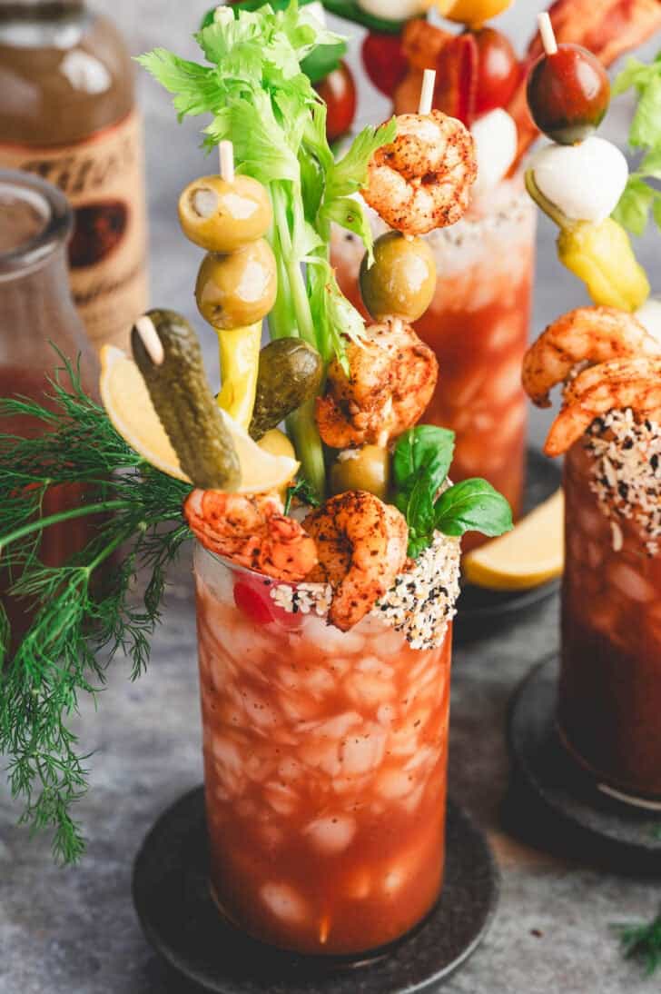 A bloody mary with lots of bloody mary garnish skewers in it.
