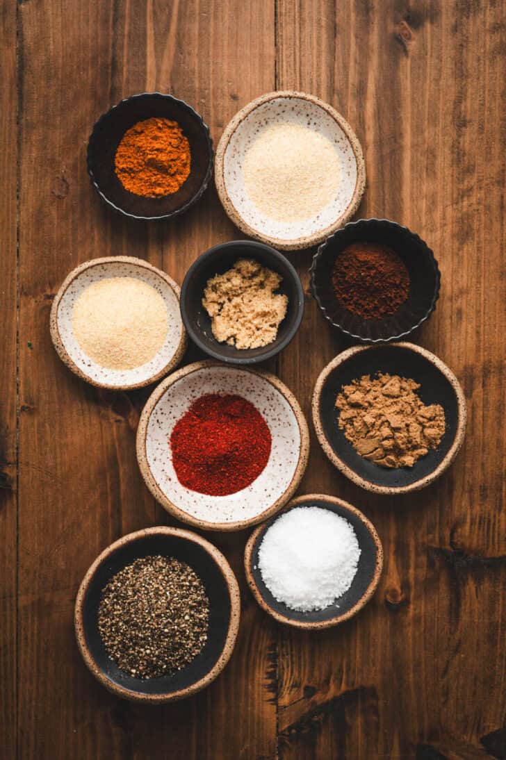 Small bowls of different spices on a wooden background.