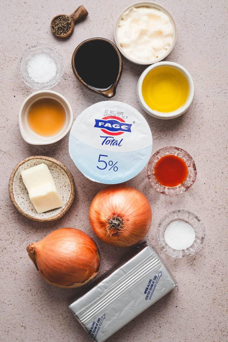 Ingredients on a light surface, including onions, cream cheese, yogurt, butter, condiments and spices.