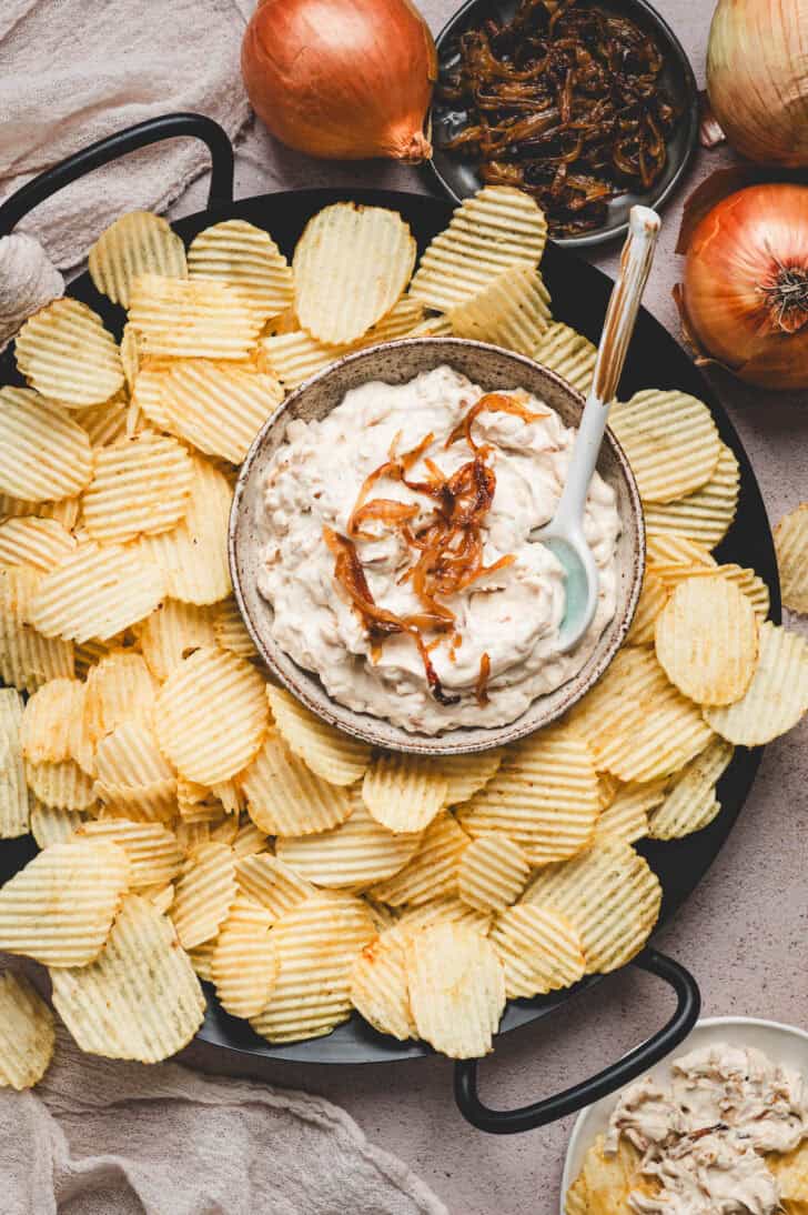 A bowl of caramelized French onion dip surrounded by potato chips.