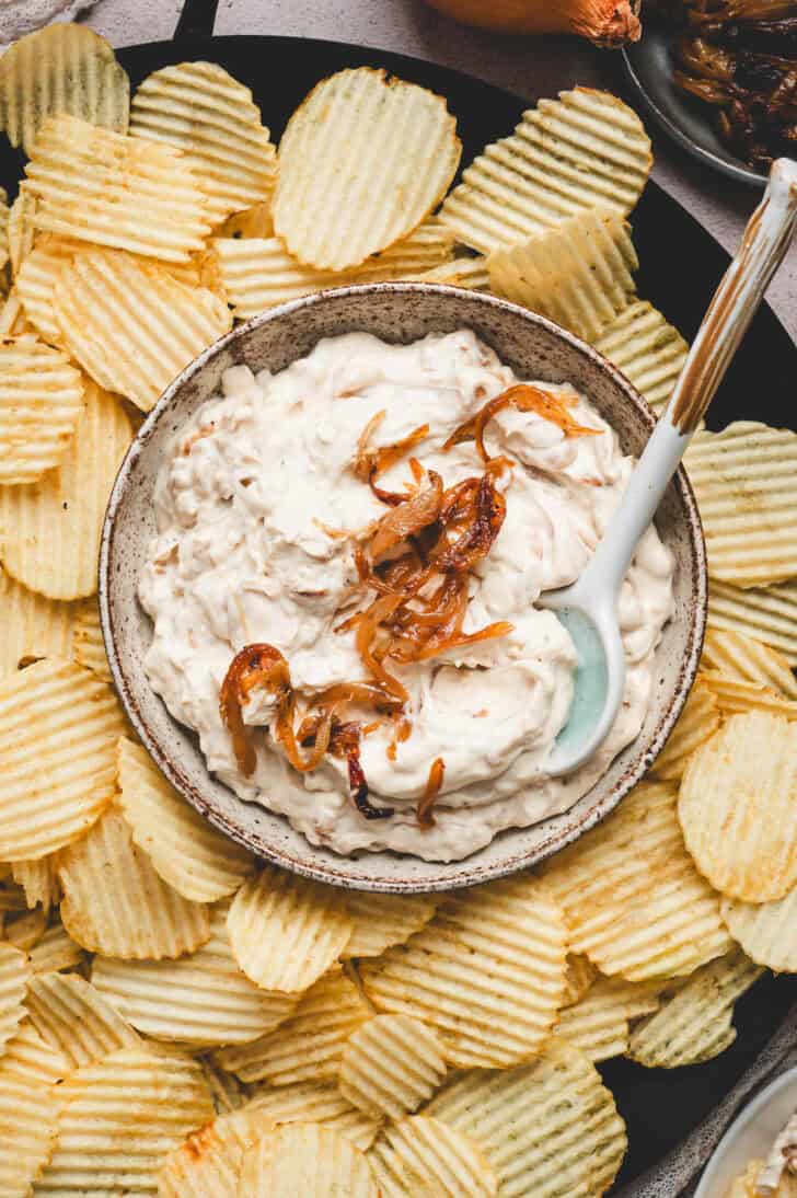 A bowl of French onion dip surrounded by potato chips.