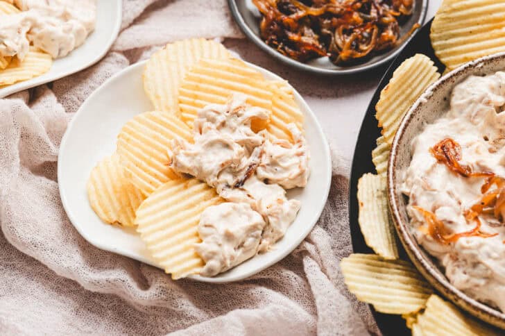 A plate filled with potato chips dipped in onion dip with caramelized onions.