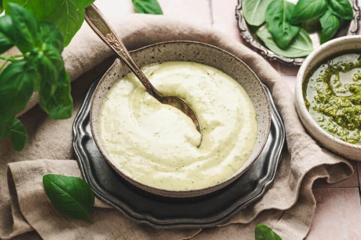 A bowl of pesto ranch with a spoon in it.