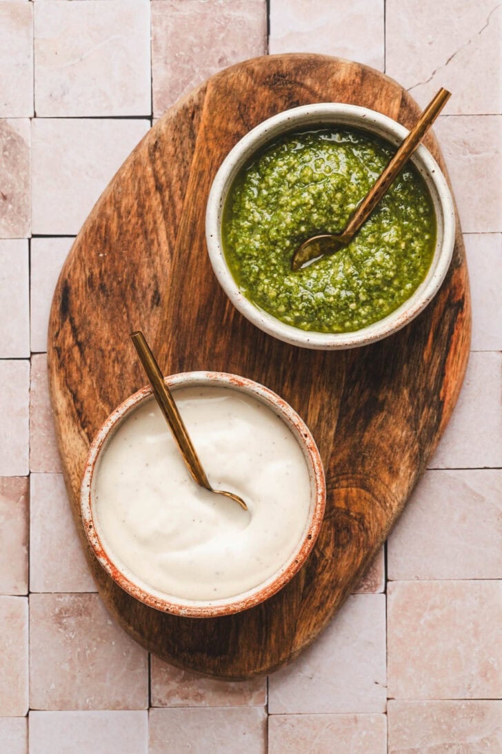 Bowls of basil pesto and ranch dressing on a wooden board.
