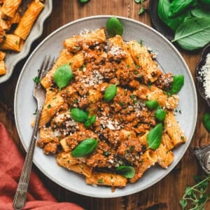A gray plate filled with rigatoni bolognese, garnished with parsley.