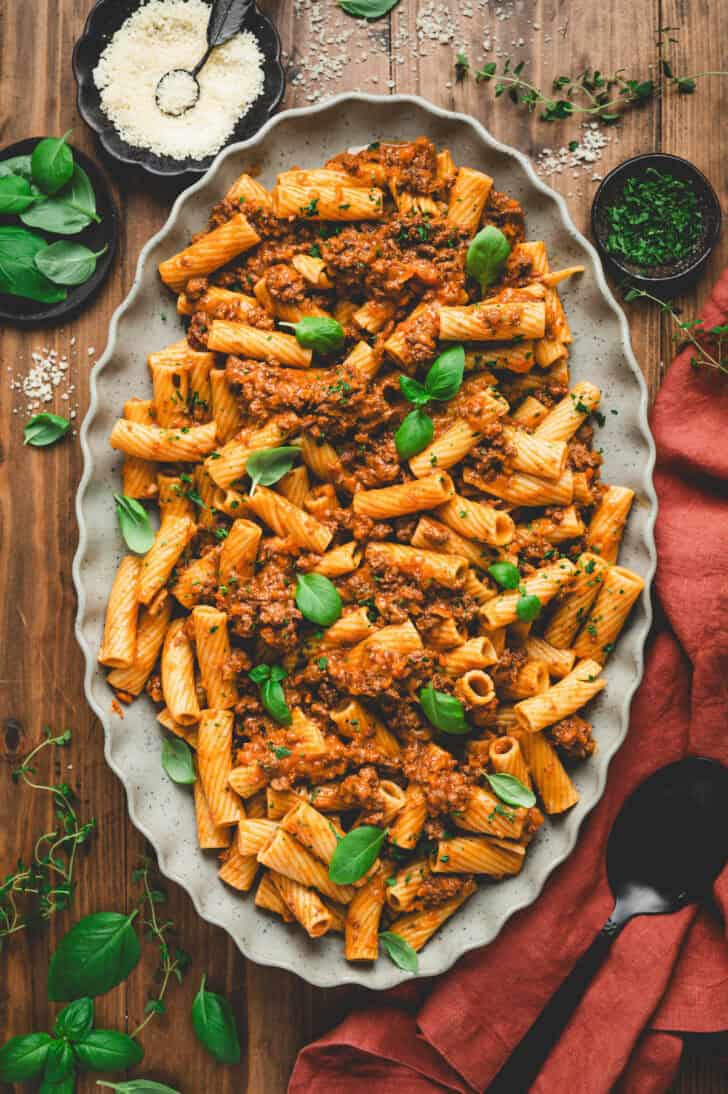 A large platter filled with rigatoni bolognese, garnished with basil leaves.