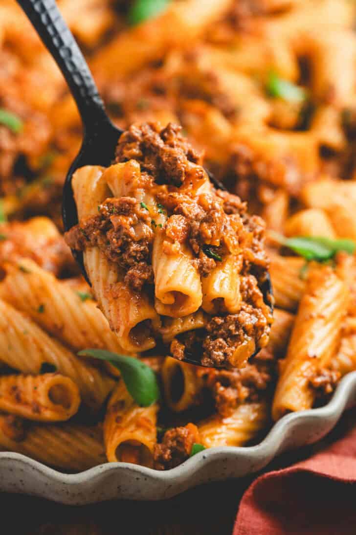 A closeup on a spoon filled with pasta and meaty red sauce.