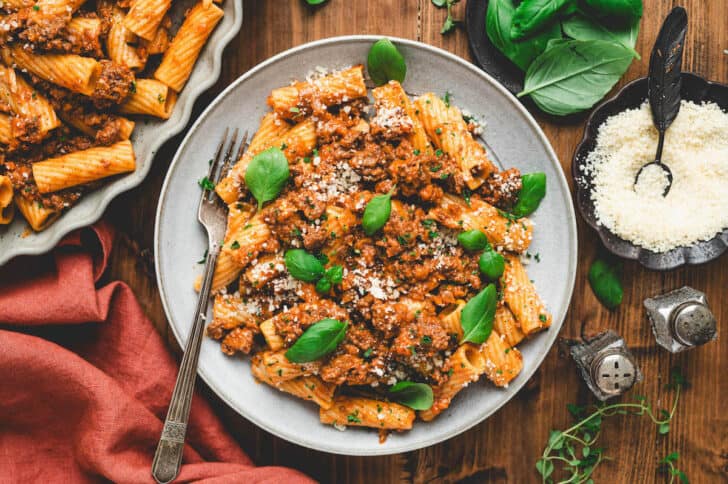 A gray plate filled with bolognese rigatoni, garnished with parsley.