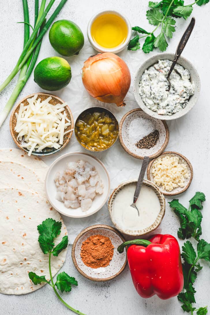 Ingredients on a light background, including shrimp, red pepper, onion, limes, cheese, herbs and spices.