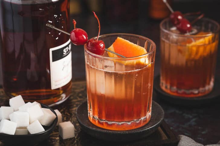 A brandy old fashioned cocktail garnished with a skewer of cherries.