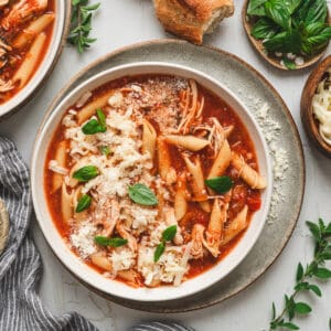 A bowl of slow cooker chicken parmesan soup on a light background.