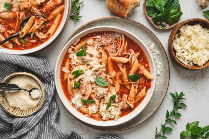 A bowl of slow cooker chicken parmesan soup on a light background.