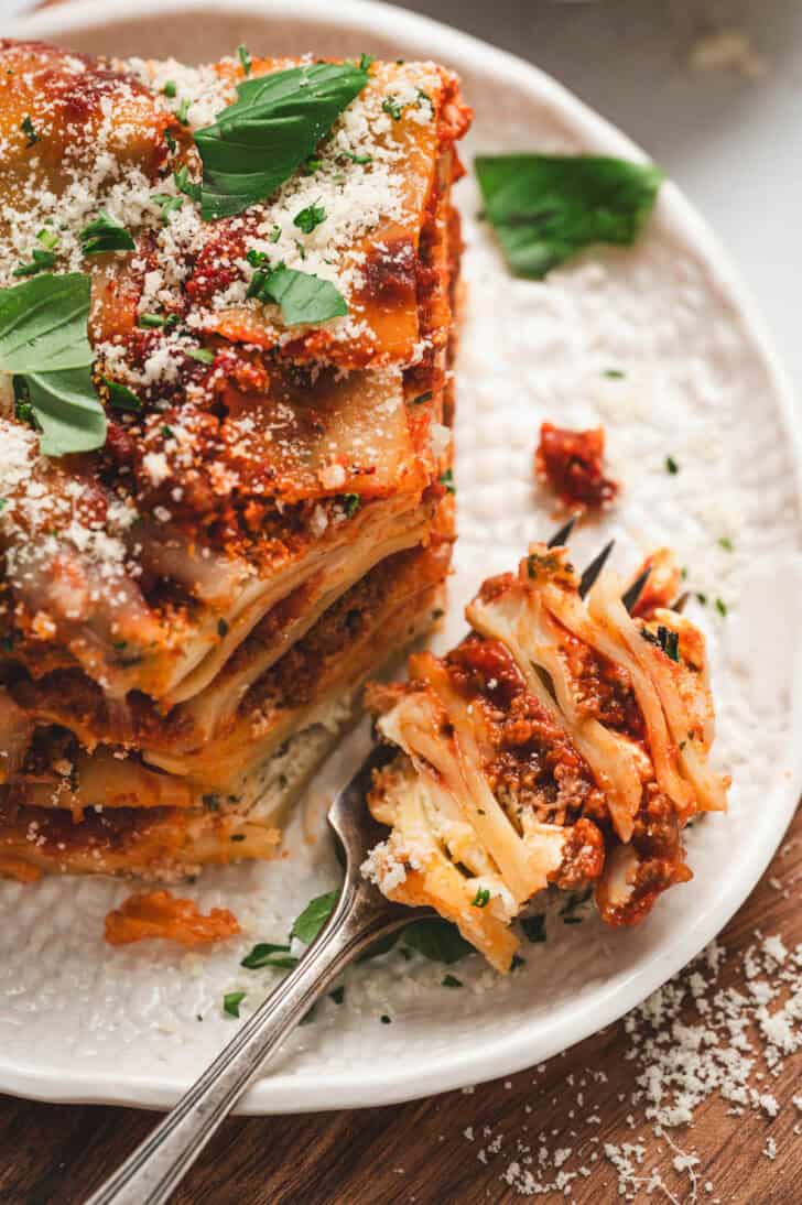 A fork with a bite of a lasagna cottage cheese recipe on it, on a white plate.