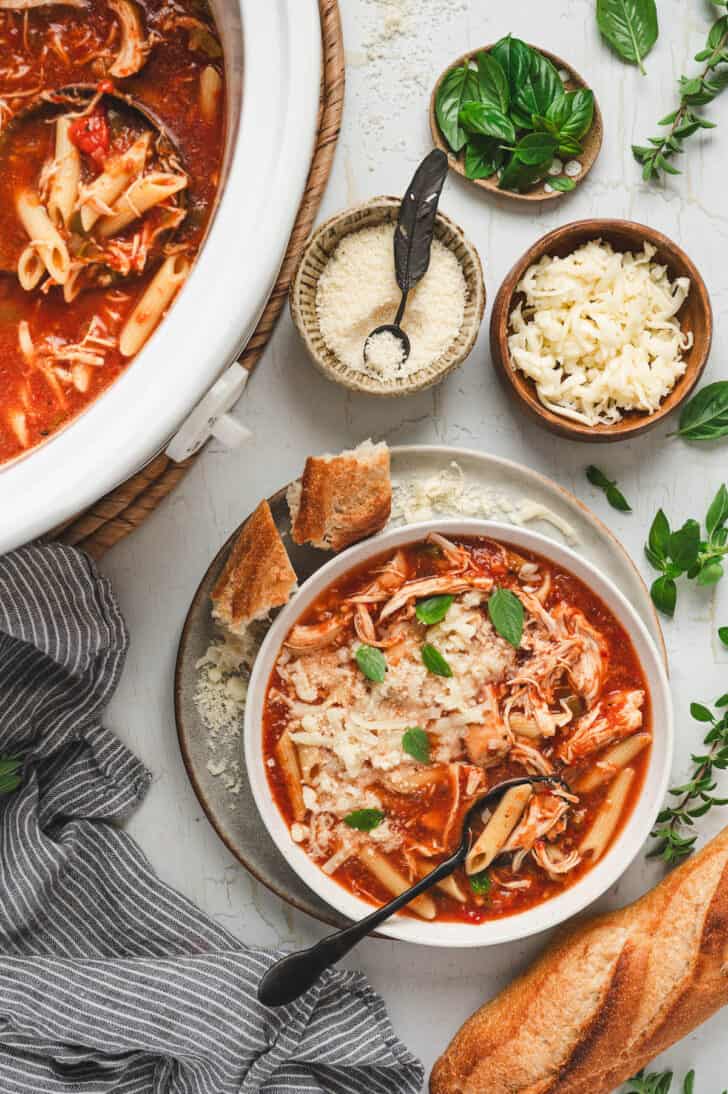 A bowl of crockpot chicken parmesan soup on a light background.