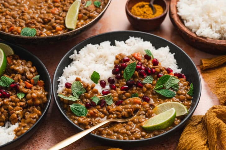 A bowl filled with rice and curry lentils, garnished with pomegranate seeds, mint leaves and lime wedges.