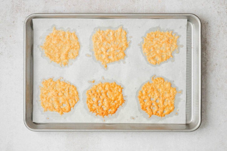 Parmesan cheese crisps on a parchment-lined rimmed baking pan.