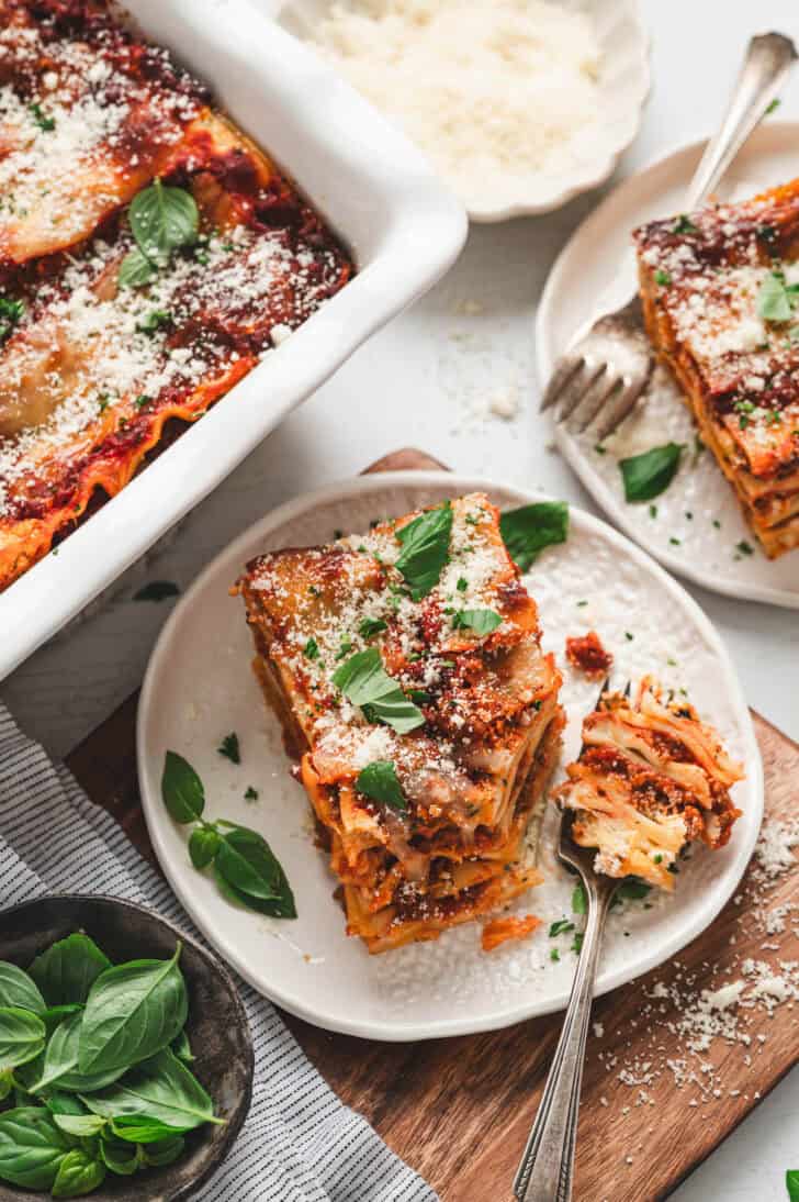 A small white plate with a piece of lasagna on it, and a fork with a bite on it.