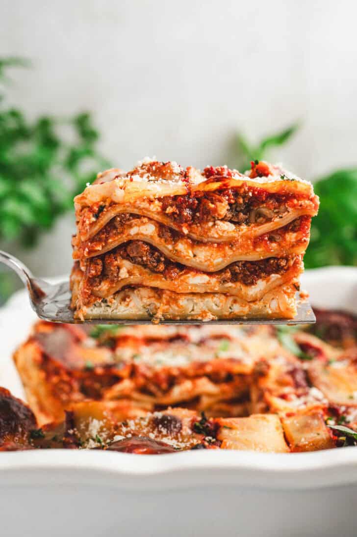 Stacked slice of lasagna made with cottage cheese and meat sauce on a spatula.