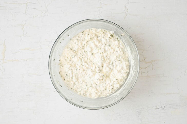 A glass bowl filled with a cottage cheese mixture on a white background.