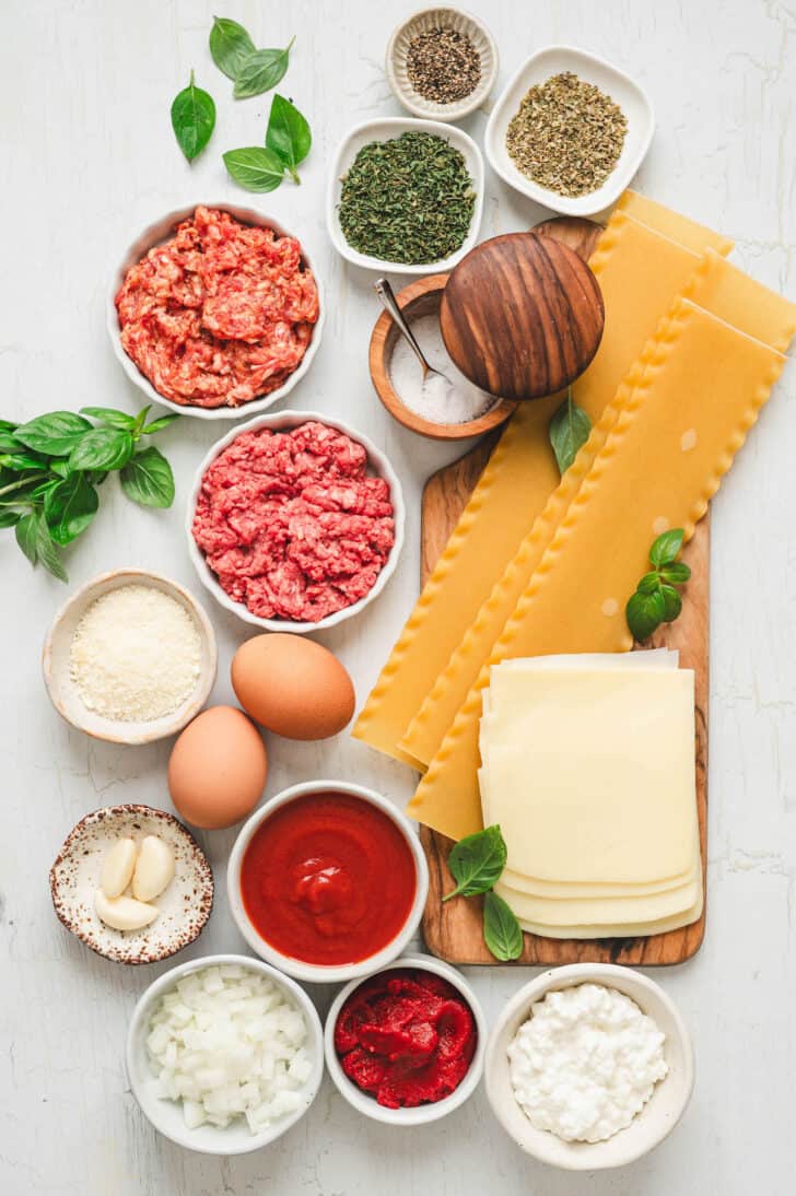 Ingredients for lasagna with cottage cheese including noodles, meat, eggs, and cheeses.
