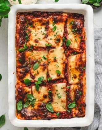 Baked cottage cheese lasagna in a white baking dish garnished with fresh basil.