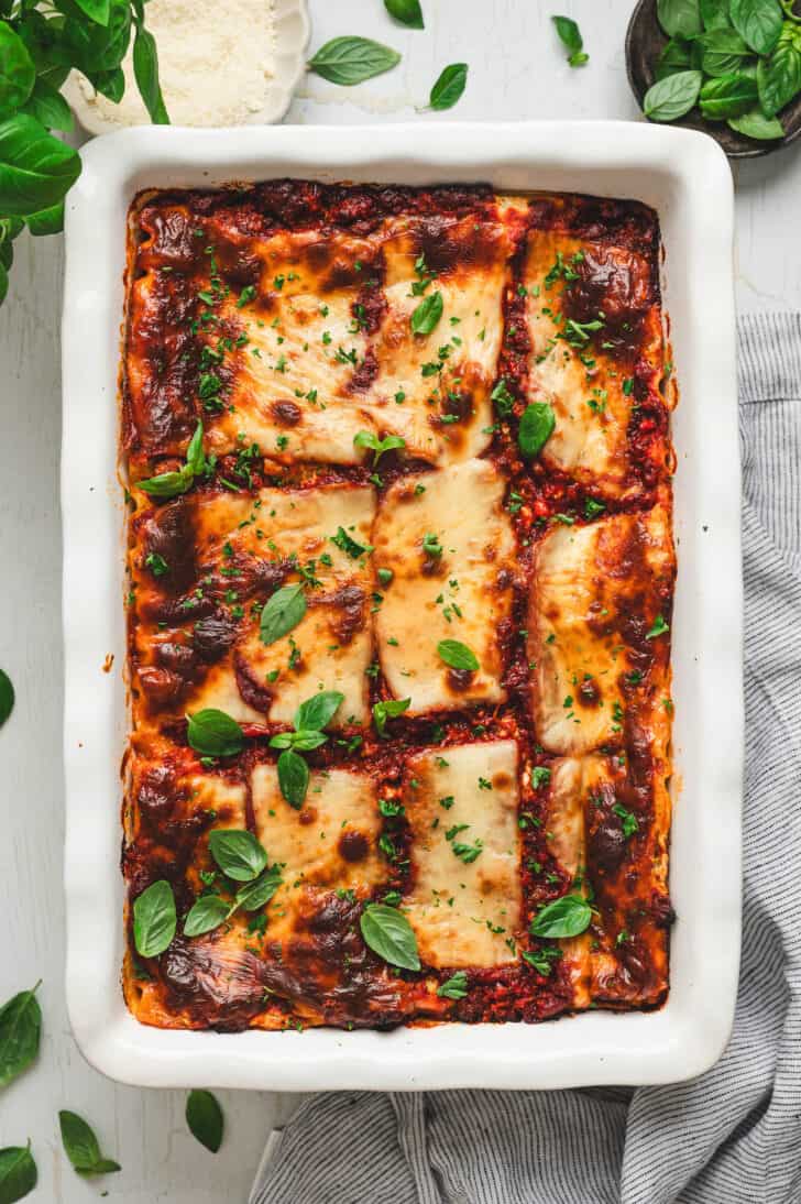 Baked cottage cheese lasagna in a white baking dish garnished with fresh basil.