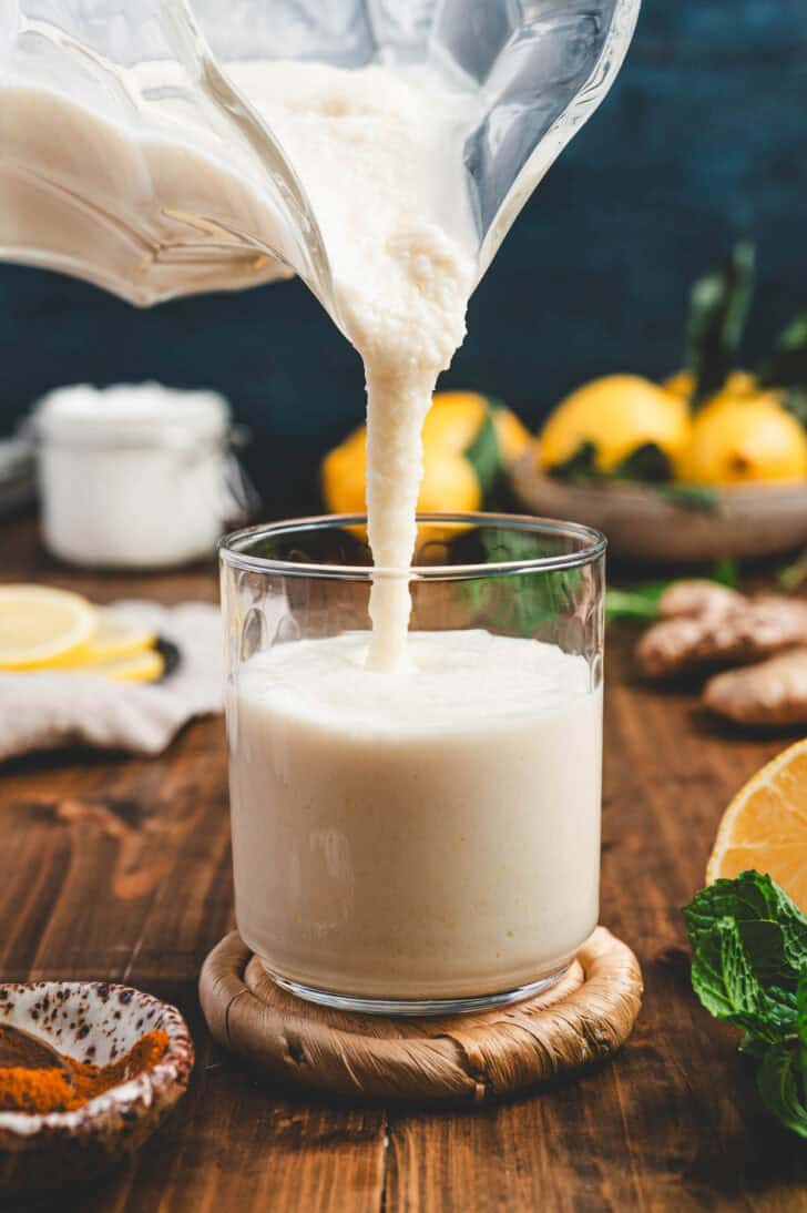 A smoothie with lemon being poured from a blender pitcher into a small glass.