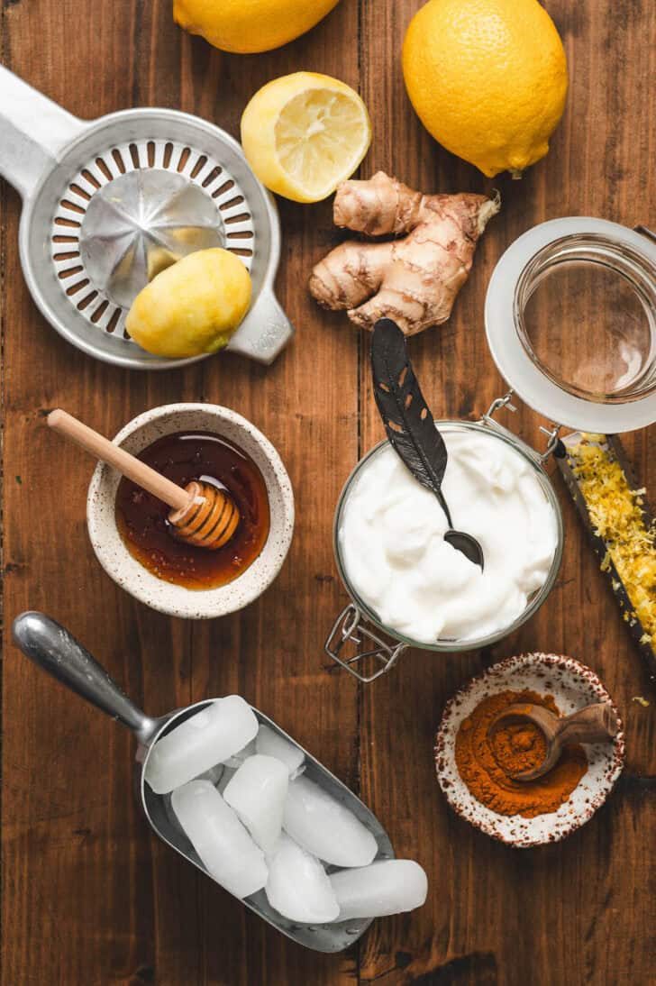Ingredients on a wooden background, including yogurt, citrus fruits, ginger, honey, spices and ice cubes.