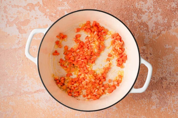 A white Dutch oven filled with sauteed chopped carrot and onion.