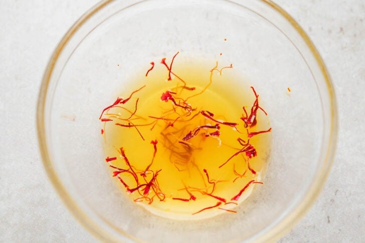 A glass bowl filled with broth and saffron threads.