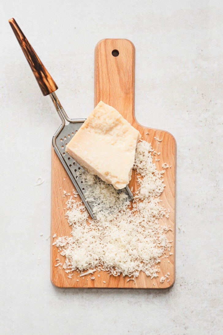 A block of Parmesan cheese being grated on a wooden cutting board.