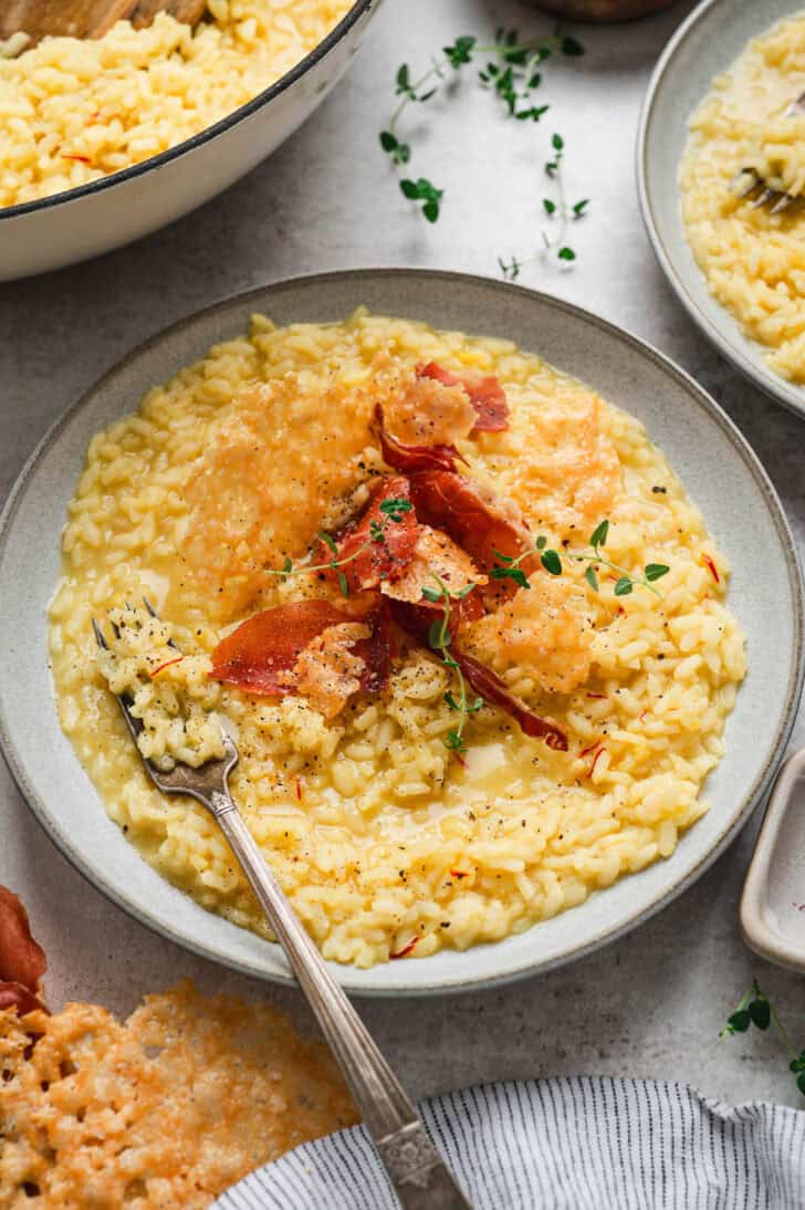 A bowl of risotto Milanese topped with crispy prosciutto and Parmesan crisps.