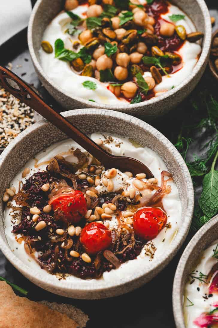 A bowl of savory yogurt topped with olive tapenade, blistered tomatoes and pine nuts.