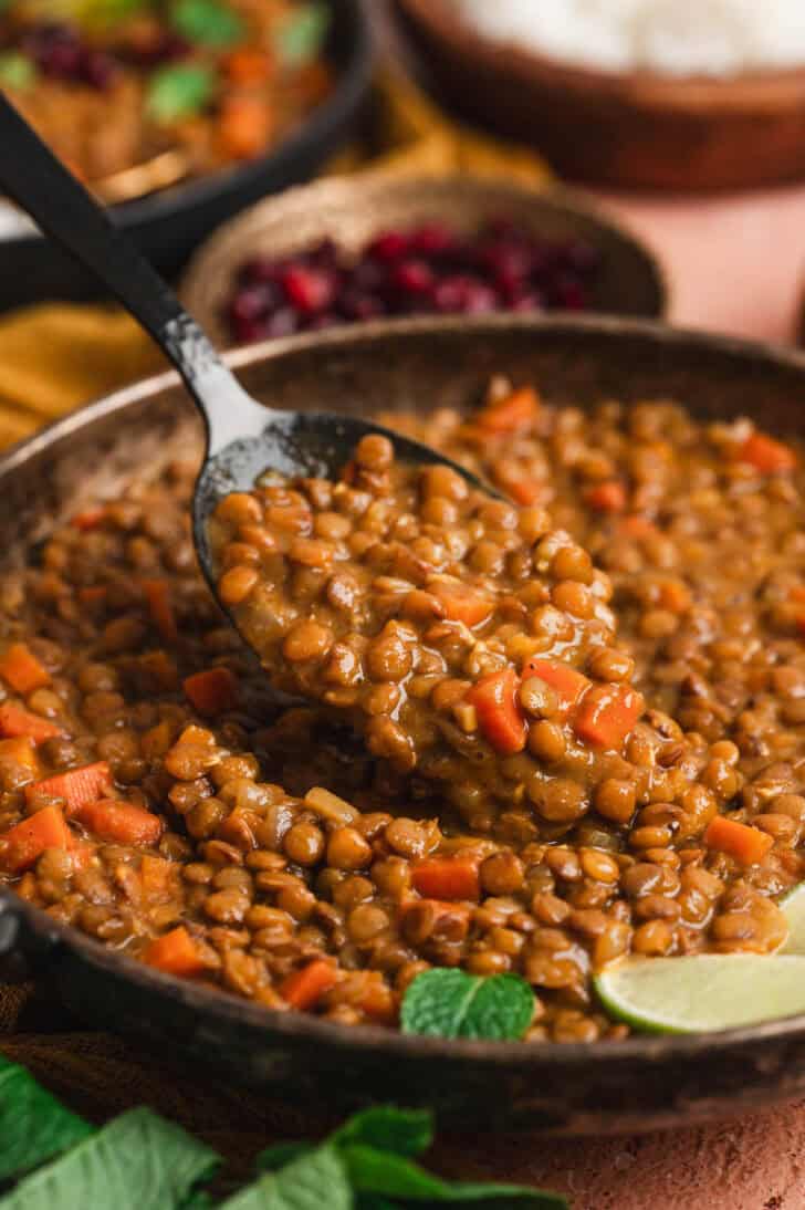 A spoon lifting a scoop of a curry lentil recipe from a serving dish.